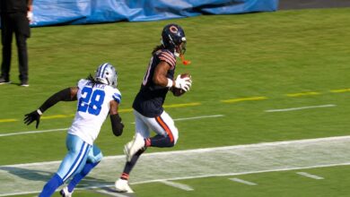Chicago Bears quarterback Caleb Williams smiles in a navy blue varsity jacket with Bears logos. Bold orange text overlay reads “THE FOUR TOUCHDOWN.” Below is dynamic game footage of a football play in progress.