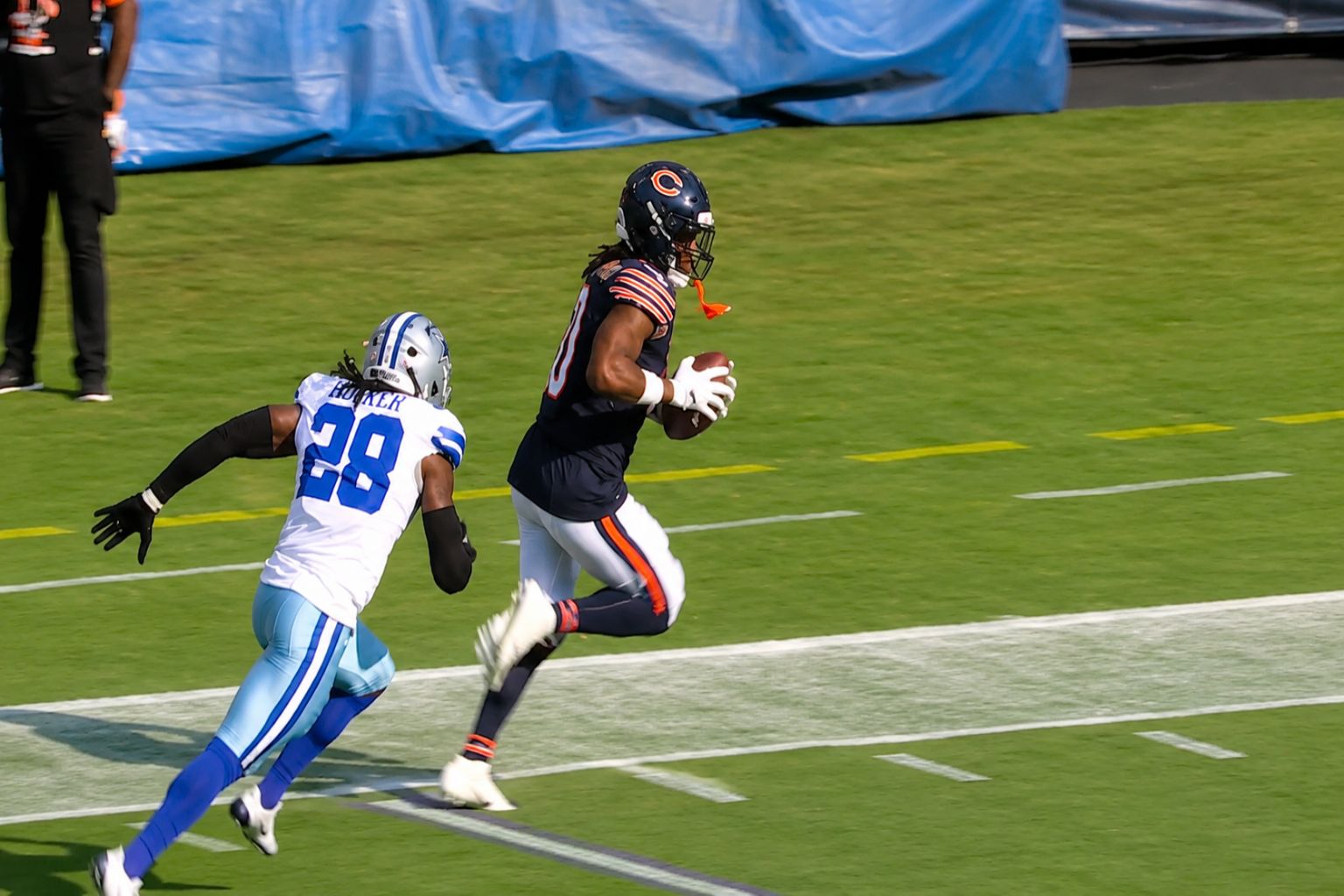 Chicago Bears quarterback Caleb Williams smiles in a navy blue varsity jacket with Bears logos. Bold orange text overlay reads “THE FOUR TOUCHDOWN.” Below is dynamic game footage of a football play in progress.